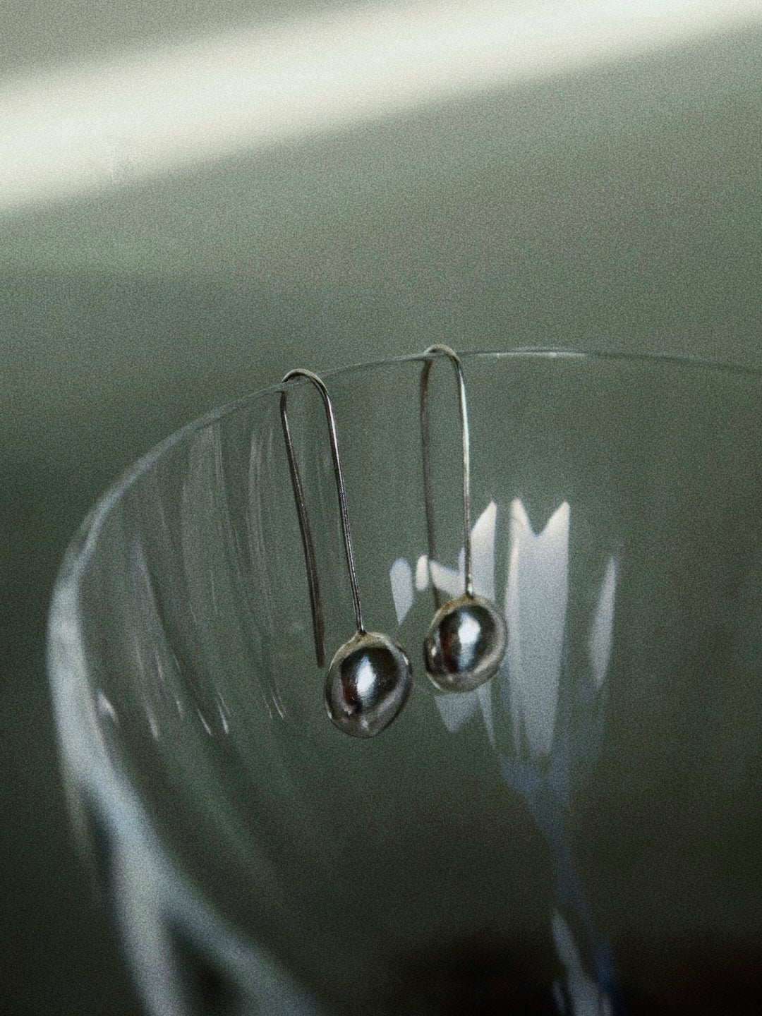 Silver earrings with teardrop-shaped beads on a reflective surface